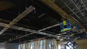 Man on scissor lift works on the ceiling of a large room with industrial roof.